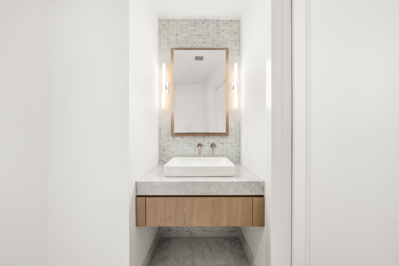 Bathroom vanity with a vessel sink, pale marble surfaces, light wood cabinetry, and tiled backsplash.