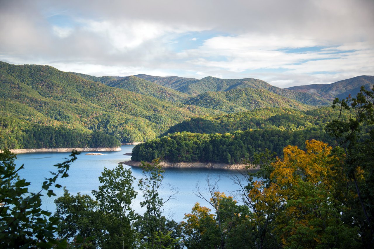 Blue reservoir winding among forested mountain ridges with early autumn foliage.