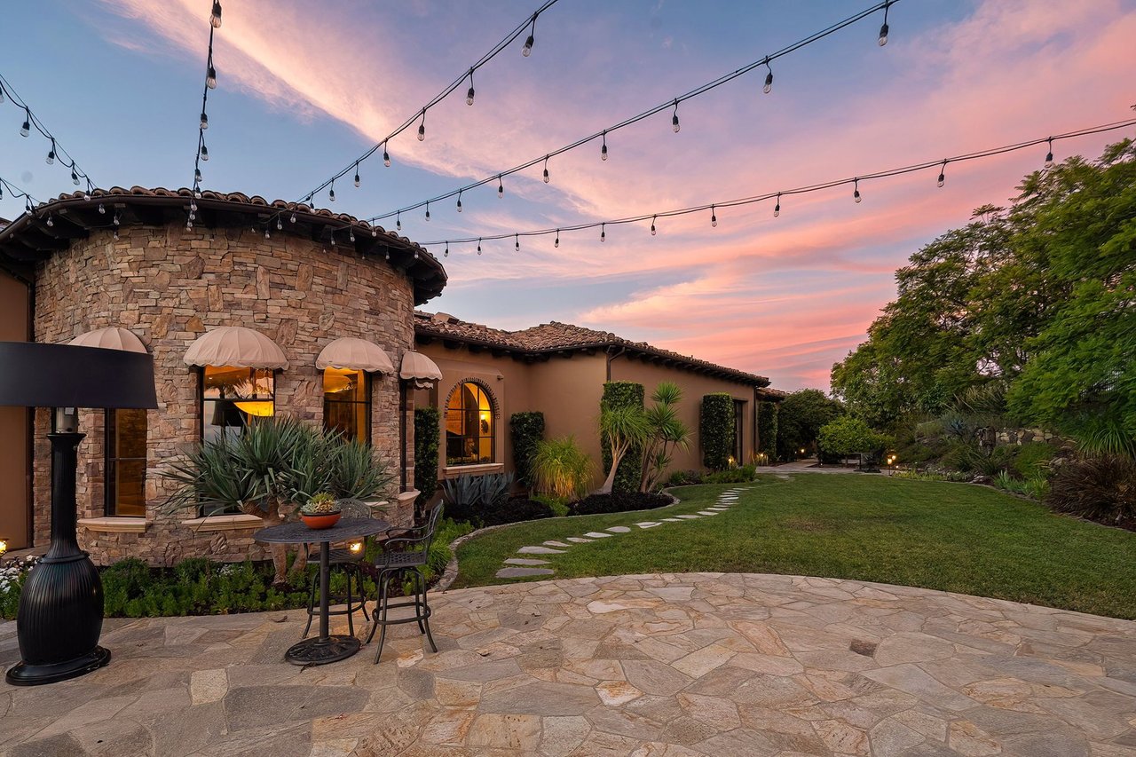 Stone home and landscaped patio beneath string lights at dusk.