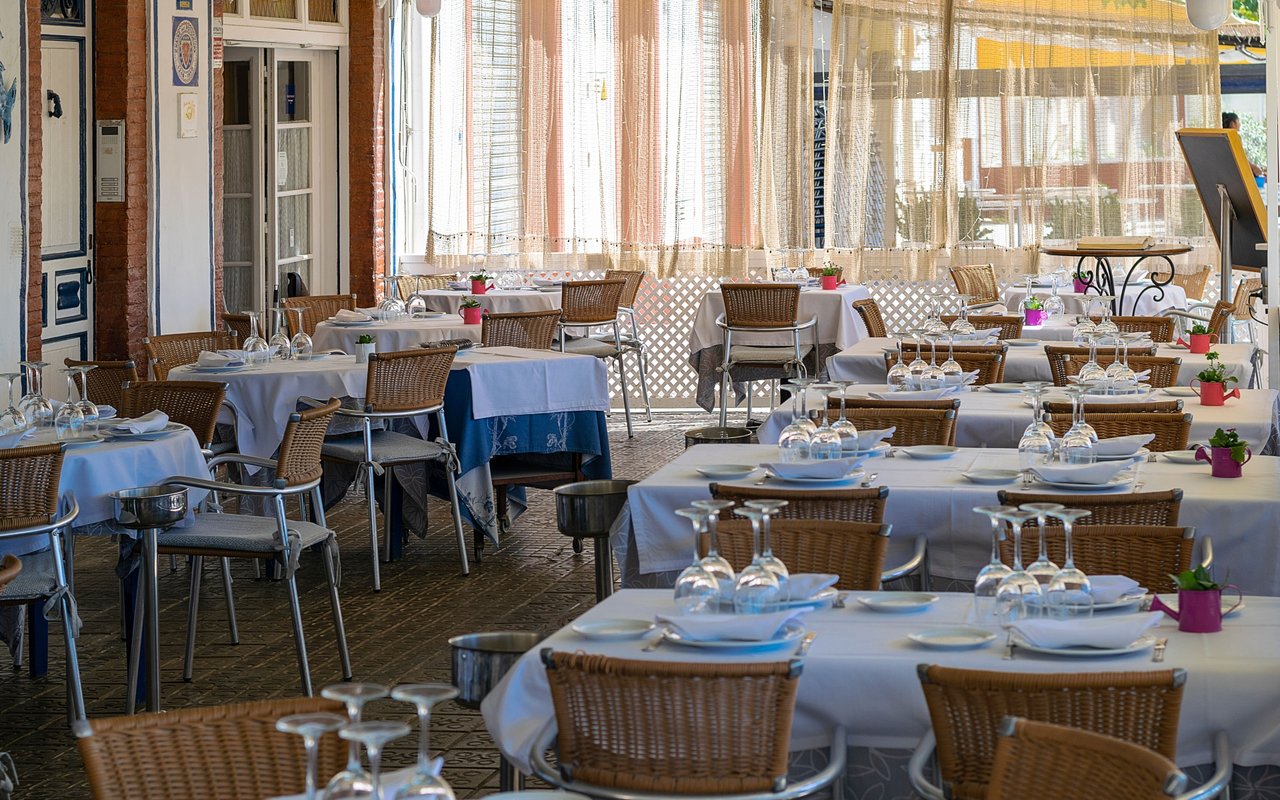 Restaurant patio lined with wicker chairs and white-clothed tables set with plates and glassware.