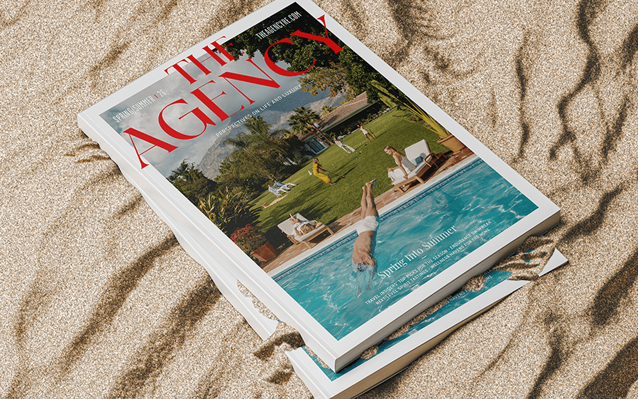 The Agency’s Spring/Summer ’26 magazine stack on sand, featuring a resort pool scene.