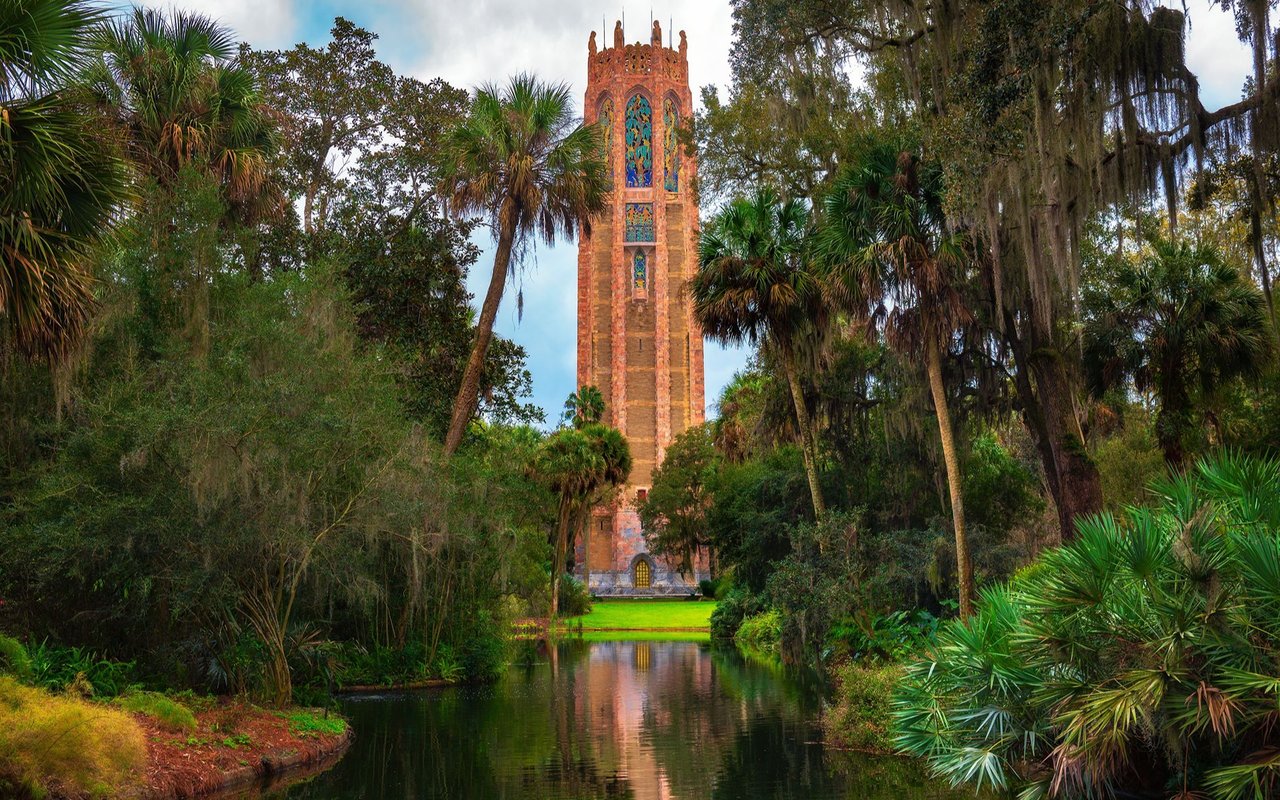 Bok Tower framed by tropical trees, reflected in a garden pond.