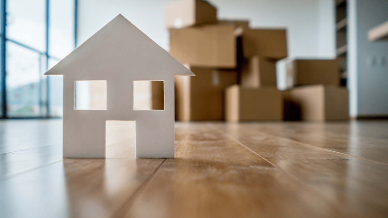 Mini house figurine on wood floor with moving boxes in background, symbolizing Gainesville FL real estate transitions. Anna Olcese Gainesville Florida Realtor