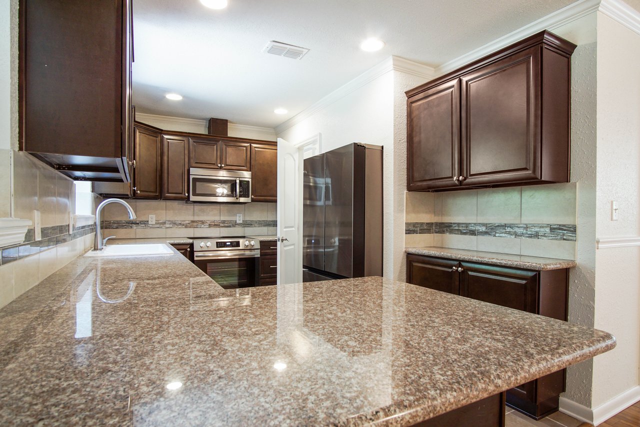 Modern kitchen with dark wood cabinets, granite countertops, stainless steel appliances, and beige tile backsplash. Bright, clean, and spacious.
