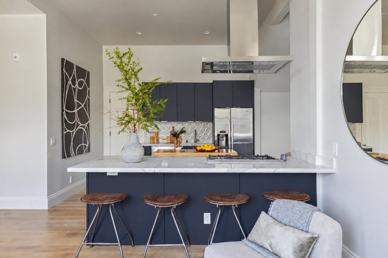 Modern kitchen with dark blue cabinets, a marble island, four stools, and a large round mirror.