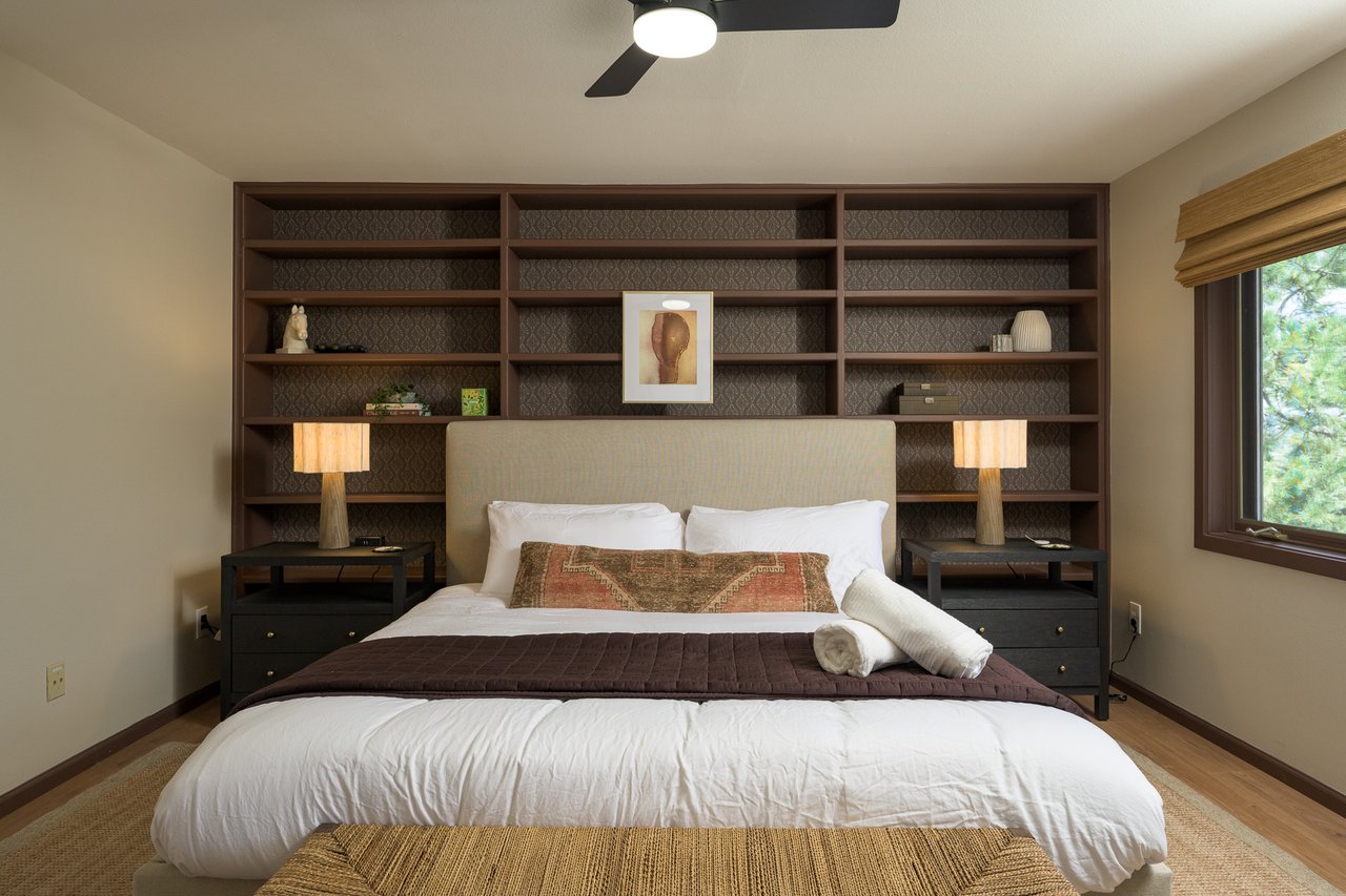 Bedroom with a bed framed by dark built-in shelves and matching bedside lamps.
