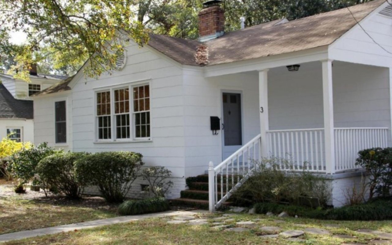 White-sided house with a covered front porch, white railings, and shrubs along the walkway.
