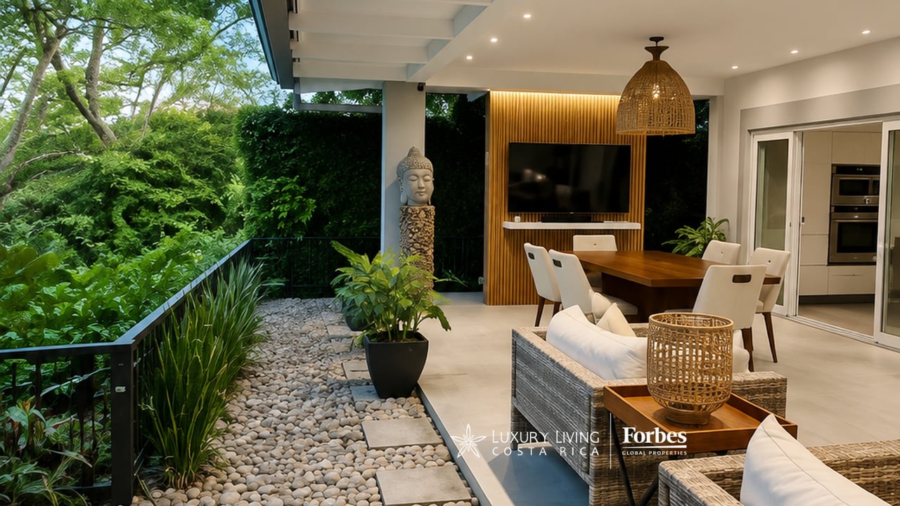 Covered terrace with dining and lounge areas beside a lush garden and stone path.