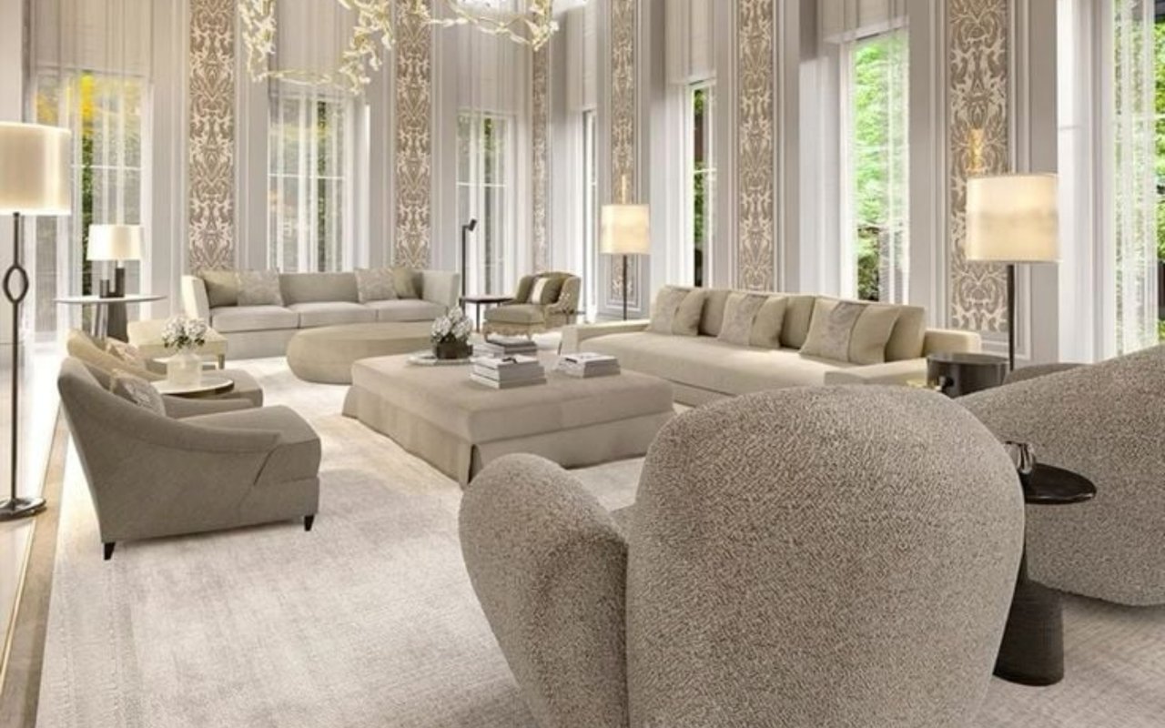 Living room with tall windows, patterned wall panels, and neutral seating around a large ottoman.