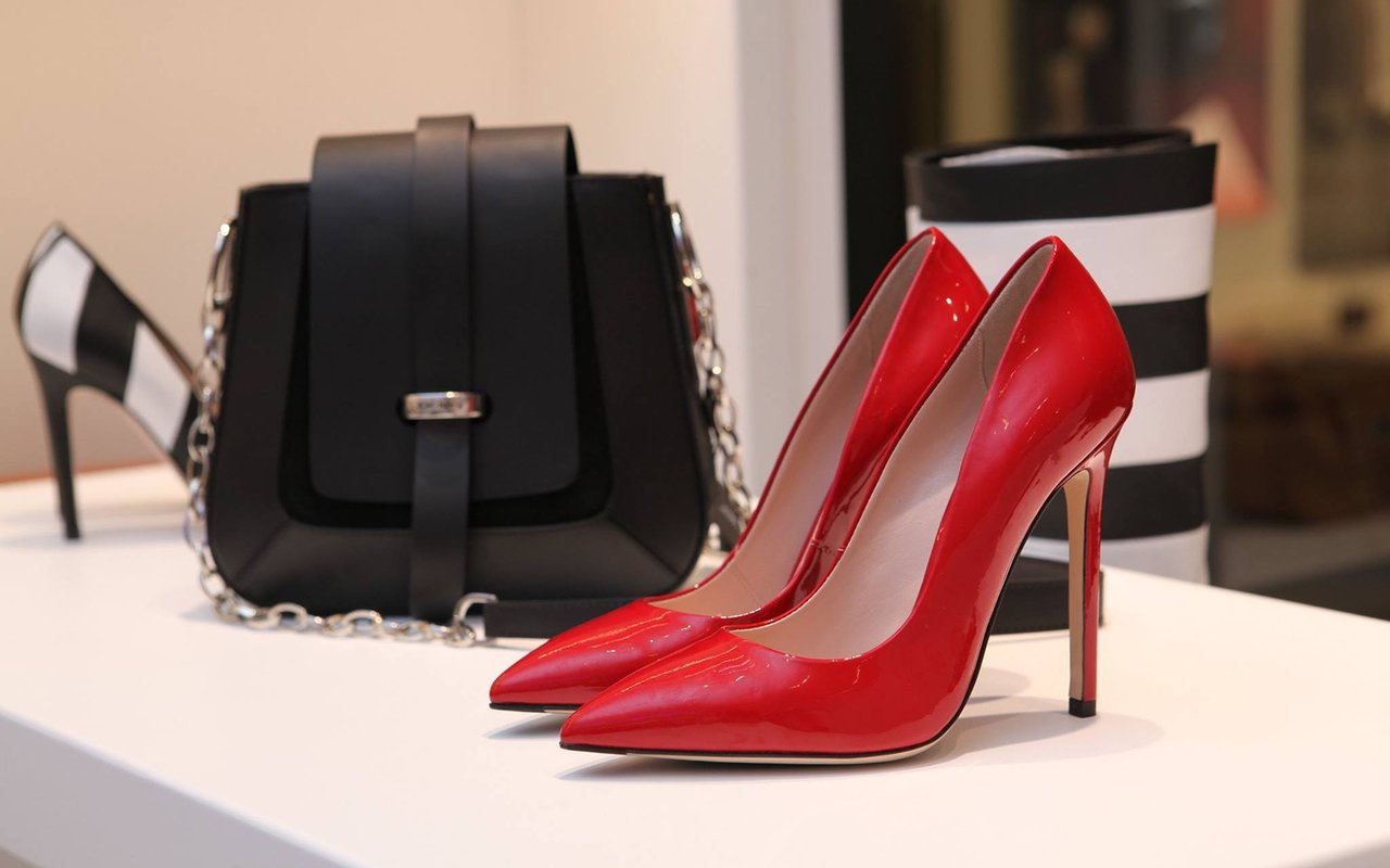 Glossy red high heels displayed beside a black handbag and striped box.