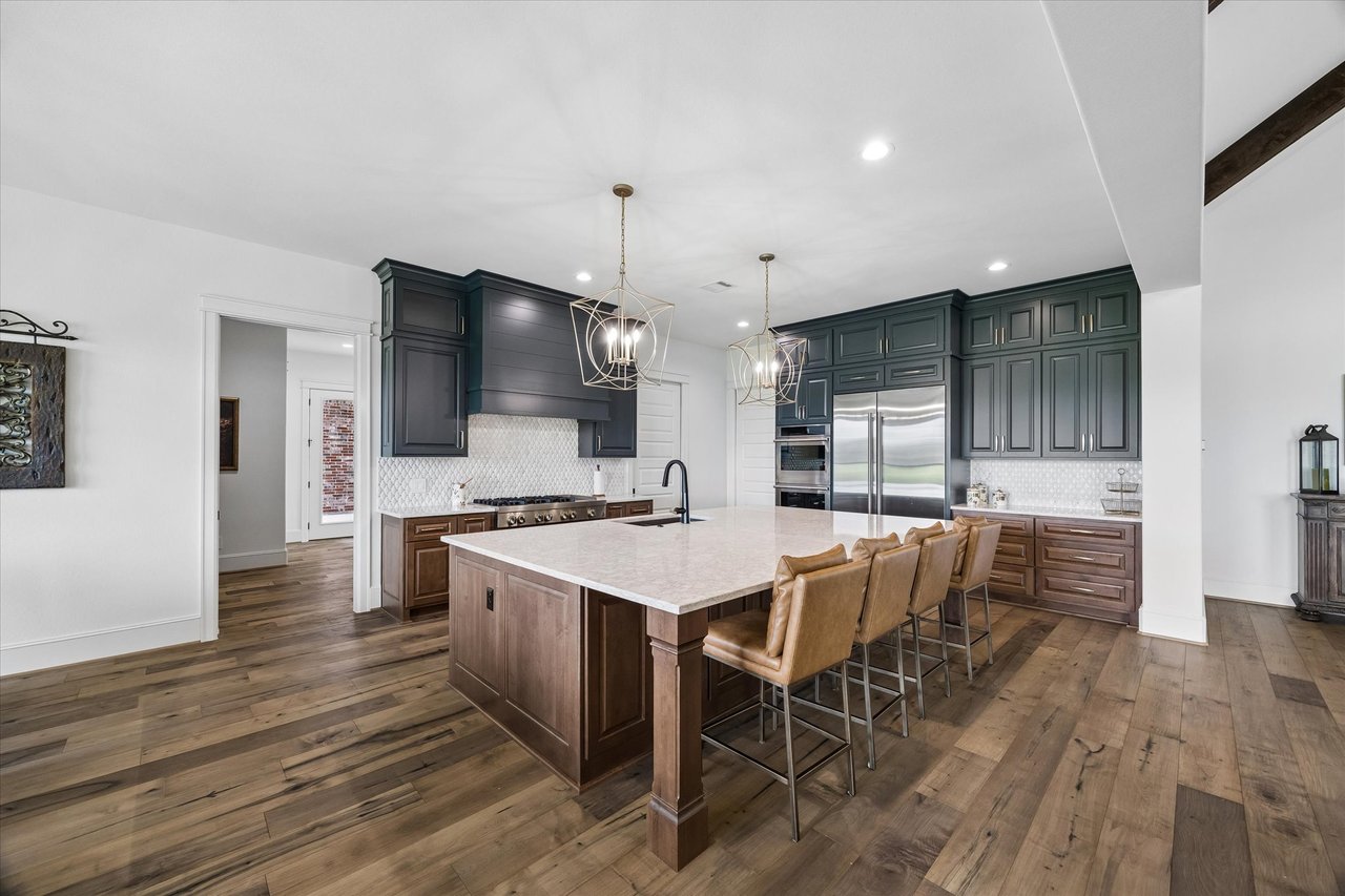 Kitchen with a large stone island, dark green cabinetry, stainless steel appliances, and wood floors.