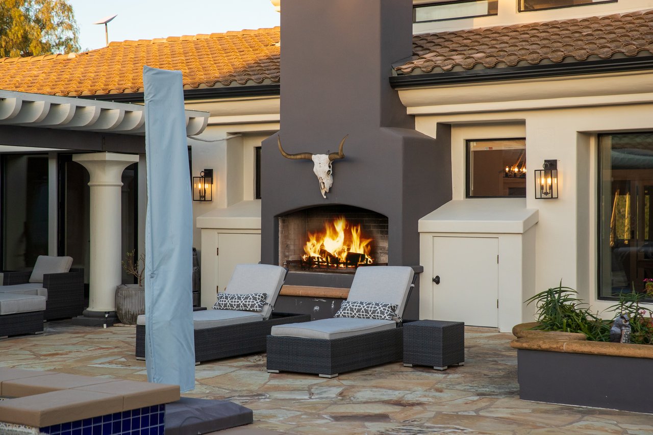 Outdoor patio with lounge chairs, a lit fireplace, and a pool edge.