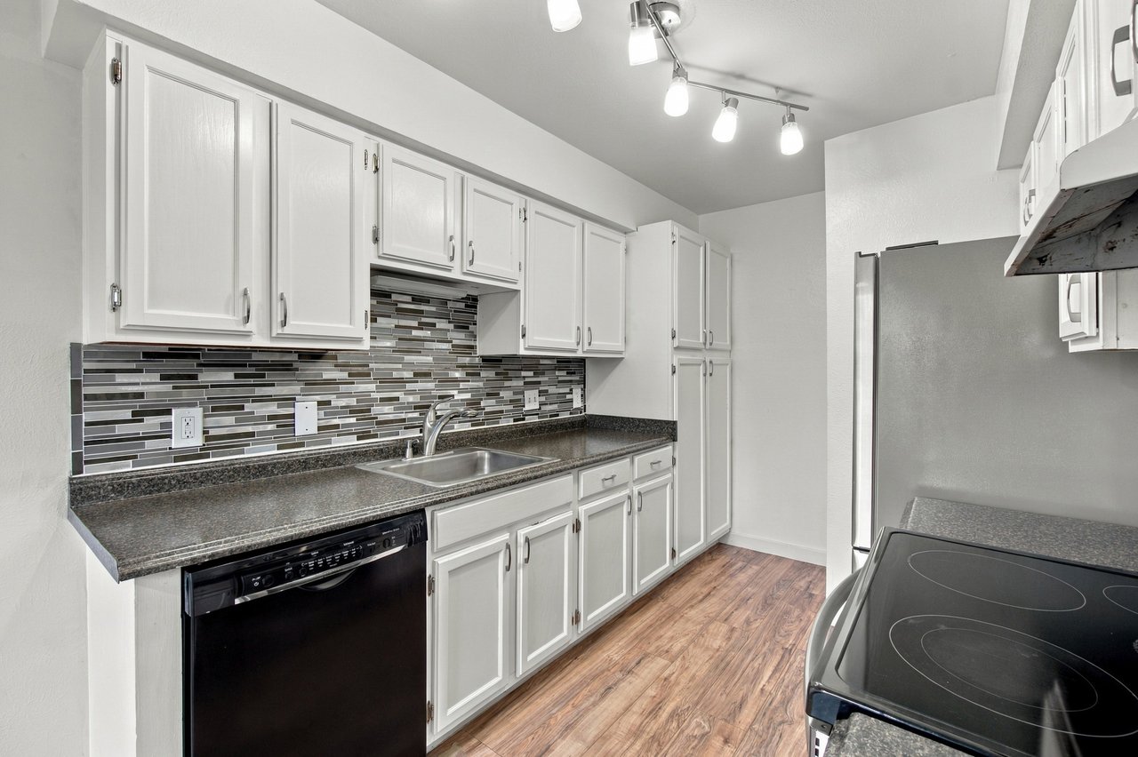 Kitchen with white cabinets, dark countertops, mosaic tile backsplash, and wood-look flooring.