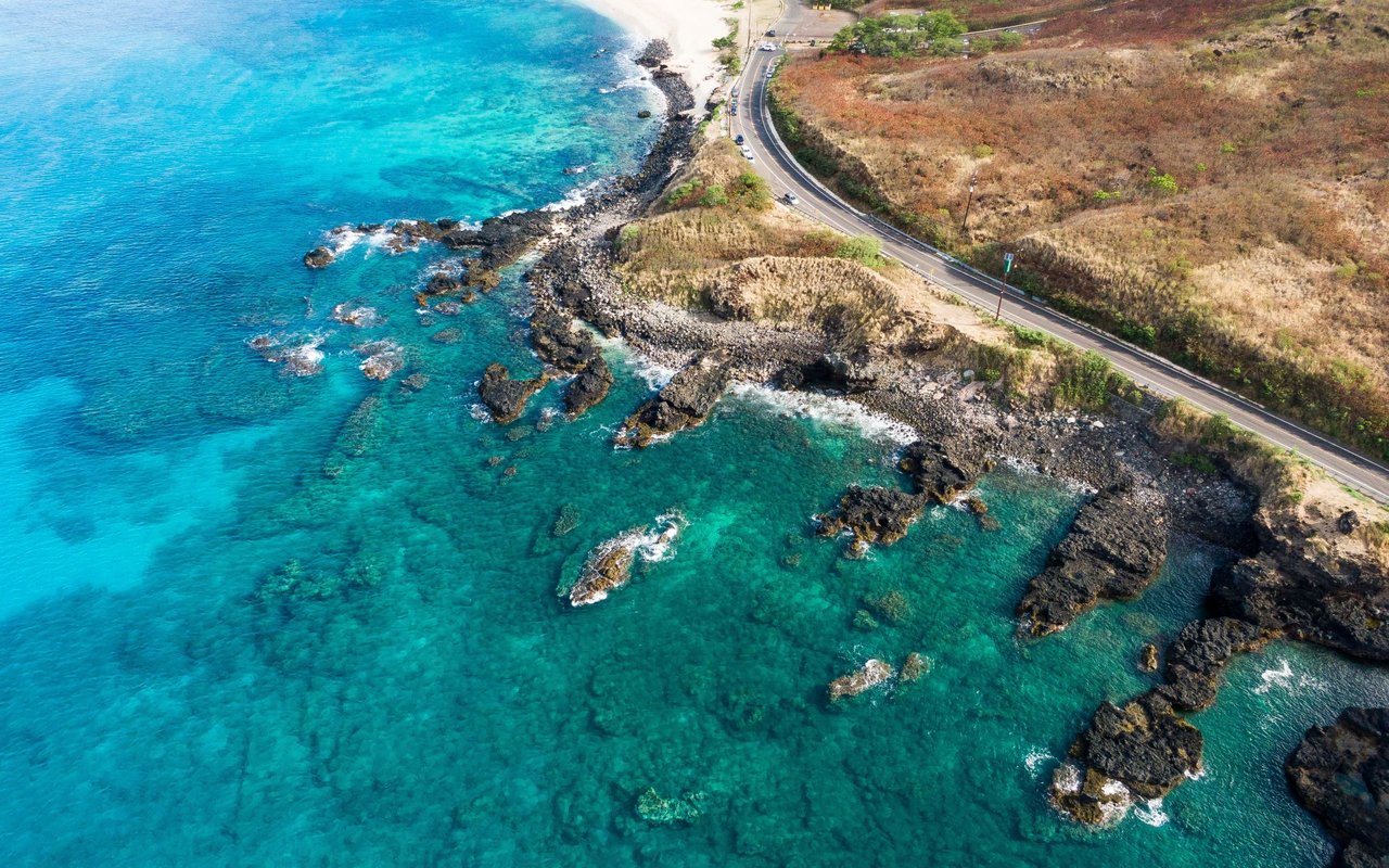 Turquoise water and rocky shoreline beside a winding coastal road in Waialua.
