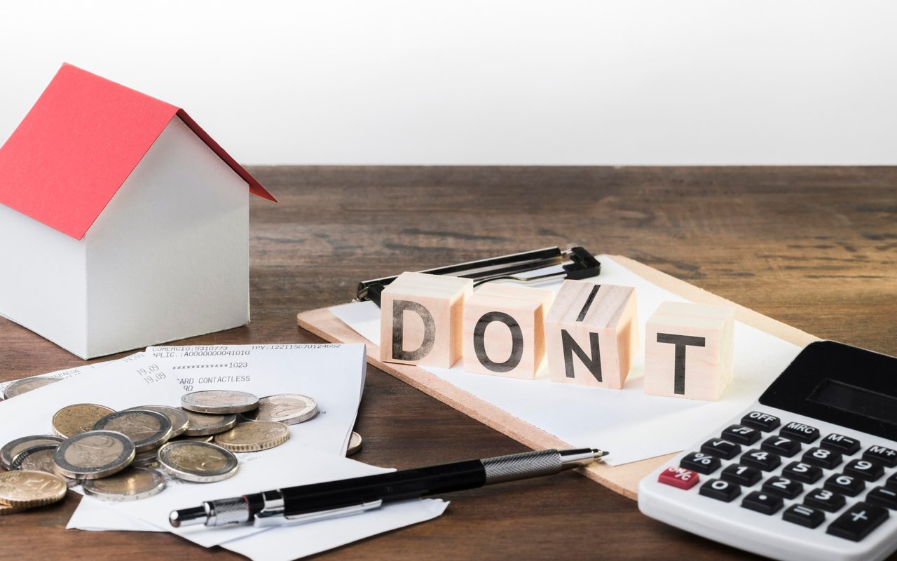 Model house, coins, and calculator beside blocks spelling “DON'T.”