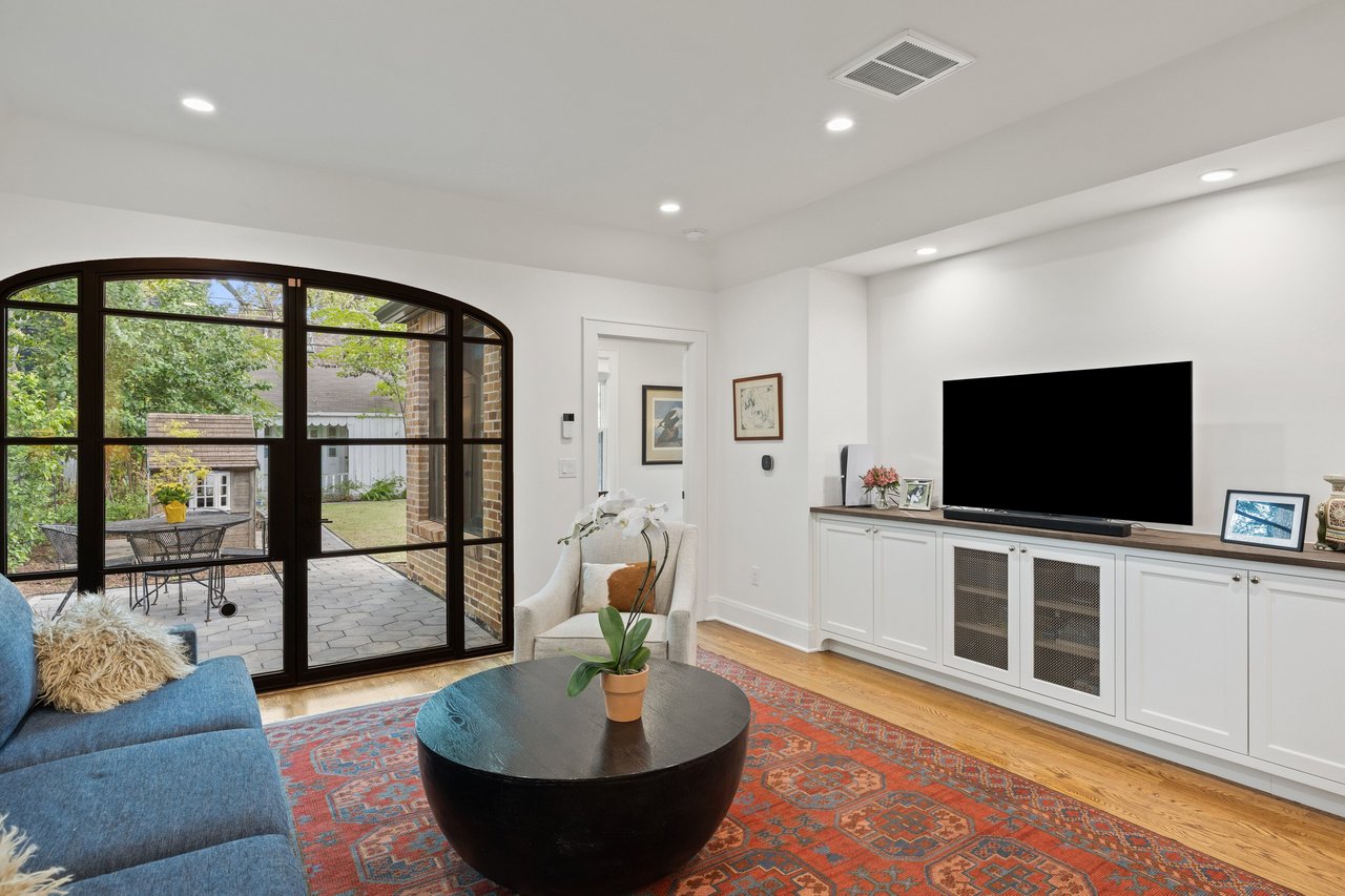 Living room with arched glass doors opening onto a leafy backyard and built-in media cabinets.