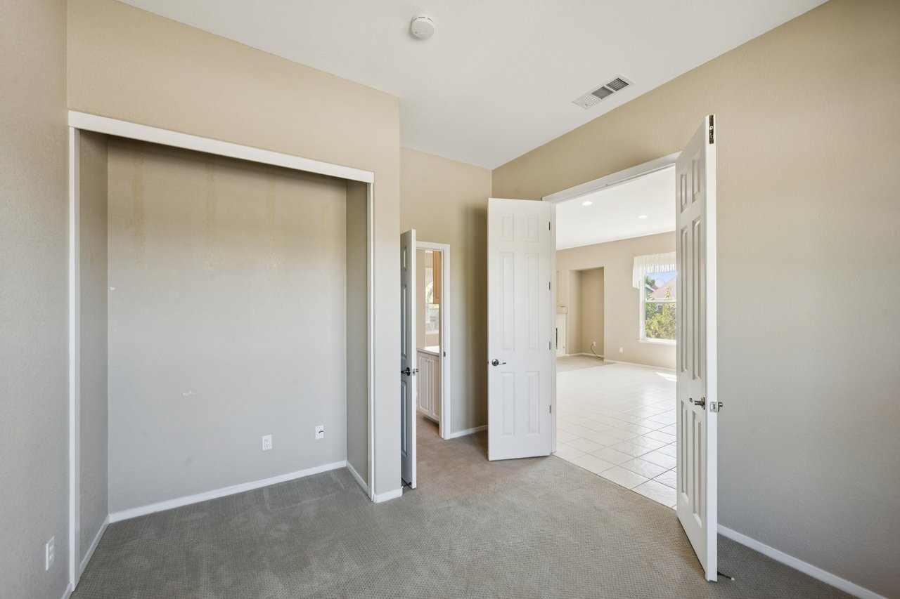 Empty carpeted bedroom with a wide closet and open doors to a bright tiled room.
