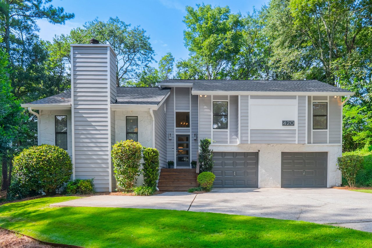 Gray-and-white split-level house with two garage doors, a tall chimney, and a landscaped front lawn.