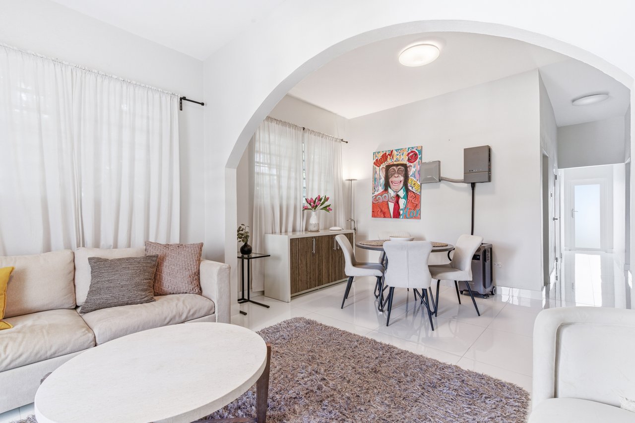 Furnished living and dining area with a broad archway and sheer curtains.