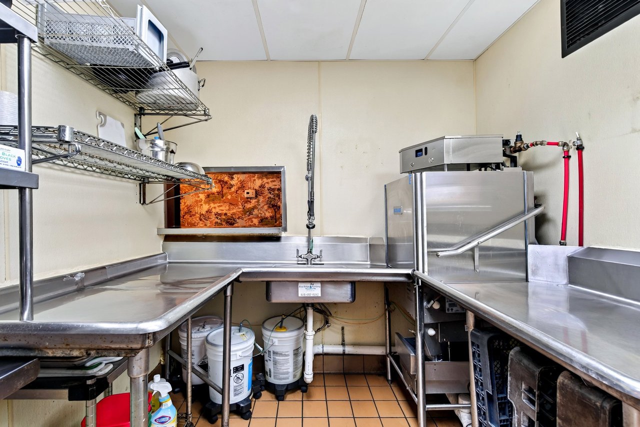Restaurant dishwashing area with stainless-steel counters, a commercial dishwasher, and wire shelving.
