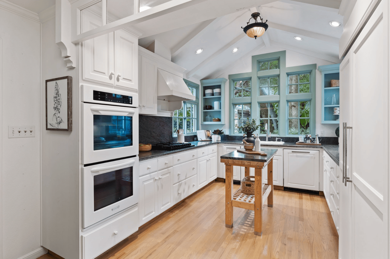 Bright kitchen with white cabinets, a central butcher-block island, and blue-green window trim.