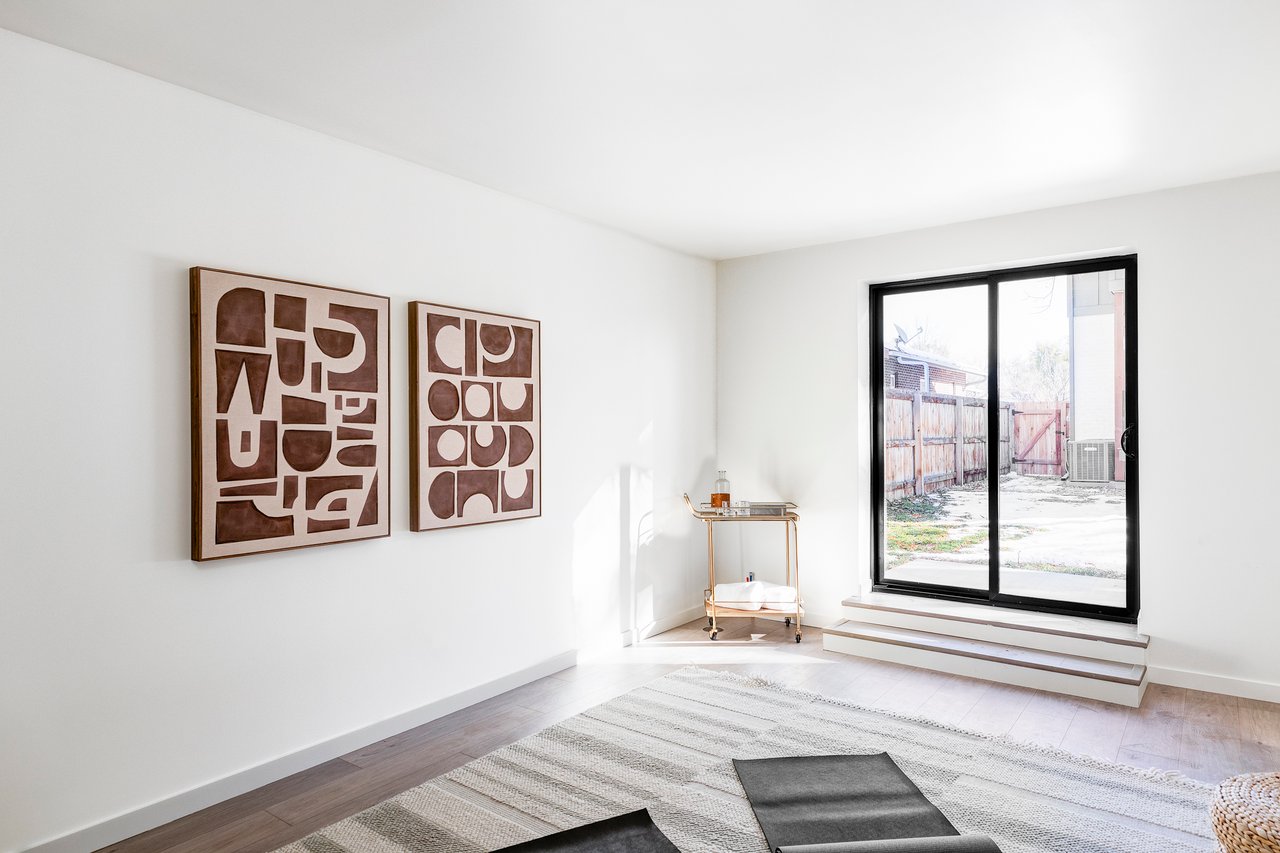 Interior image of ADU with modern artwork on the wall, a bar cart in the corner and yoga mats on the floor. Entry is a sliding glass door with two steps down.