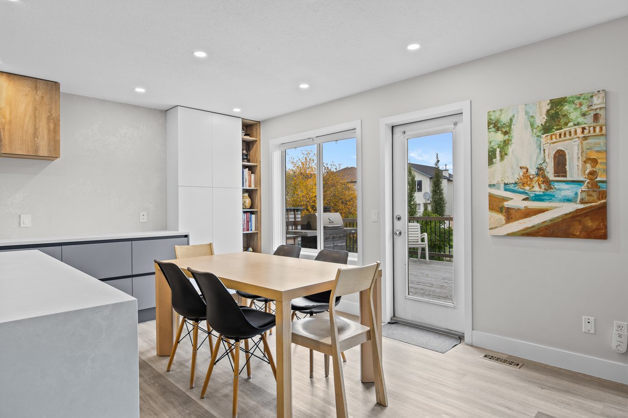 Dining area with a light wood table, mixed chairs, and a glass door opening onto a deck.