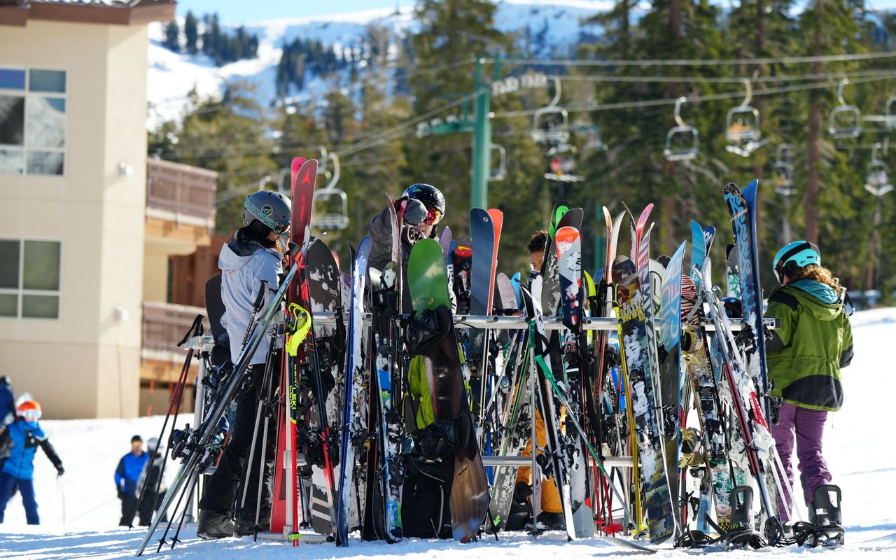 Skiers gather around colorful skis at a snowy resort beneath a chairlift.