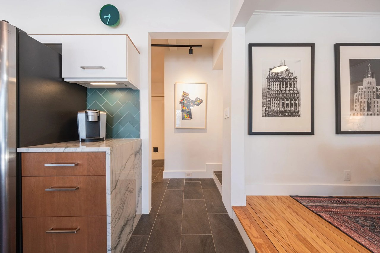 Renovated apartment kitchen with walnut drawers, marble counters, and a teal tile backsplash.