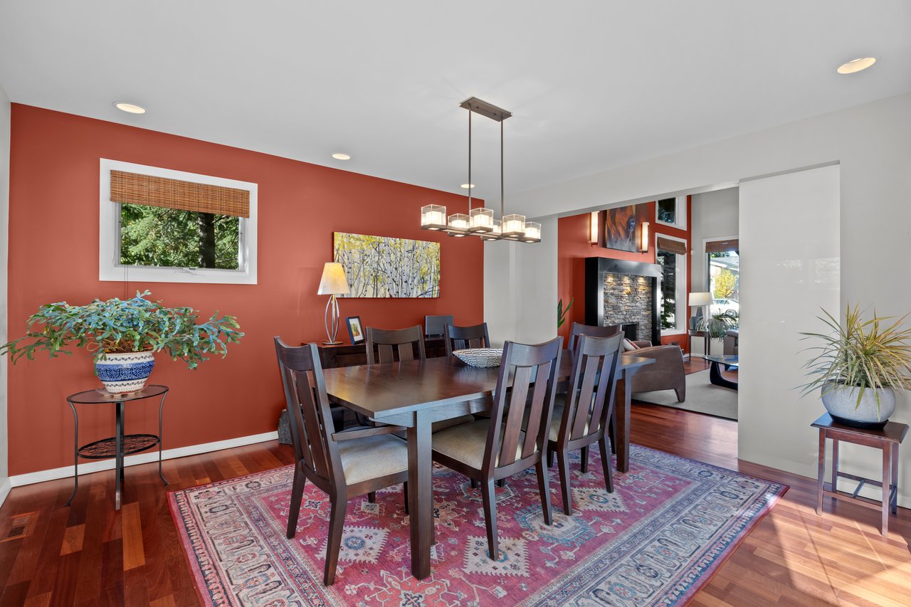 Dining room with a dark wood table on a patterned rug beside a terracotta-red accent wall.