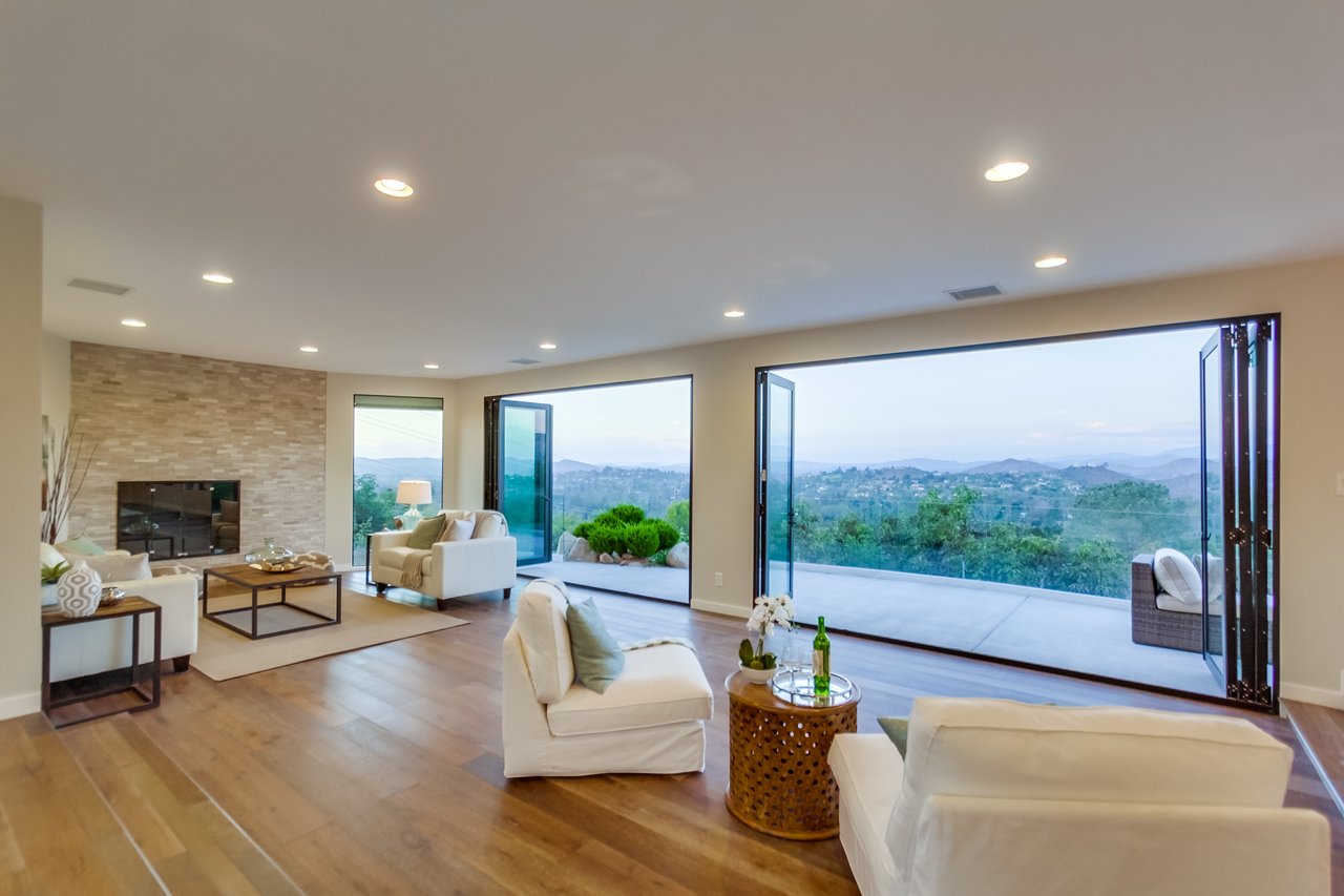 Living room with a stone fireplace and wide-open glass doors overlooking green hills.