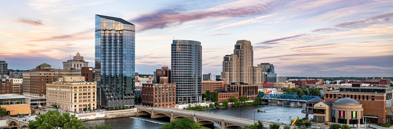 Grand Rapids skyline with modern high-rise buildings and the Grand River at sunset.