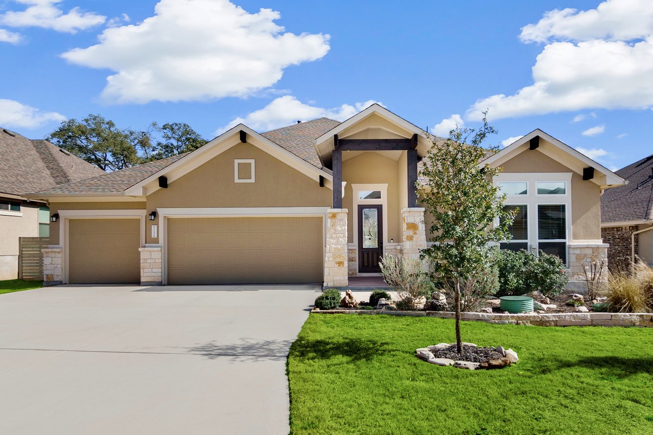 Tan single-story home with a three-car garage, stone accents, and landscaped lawn.
