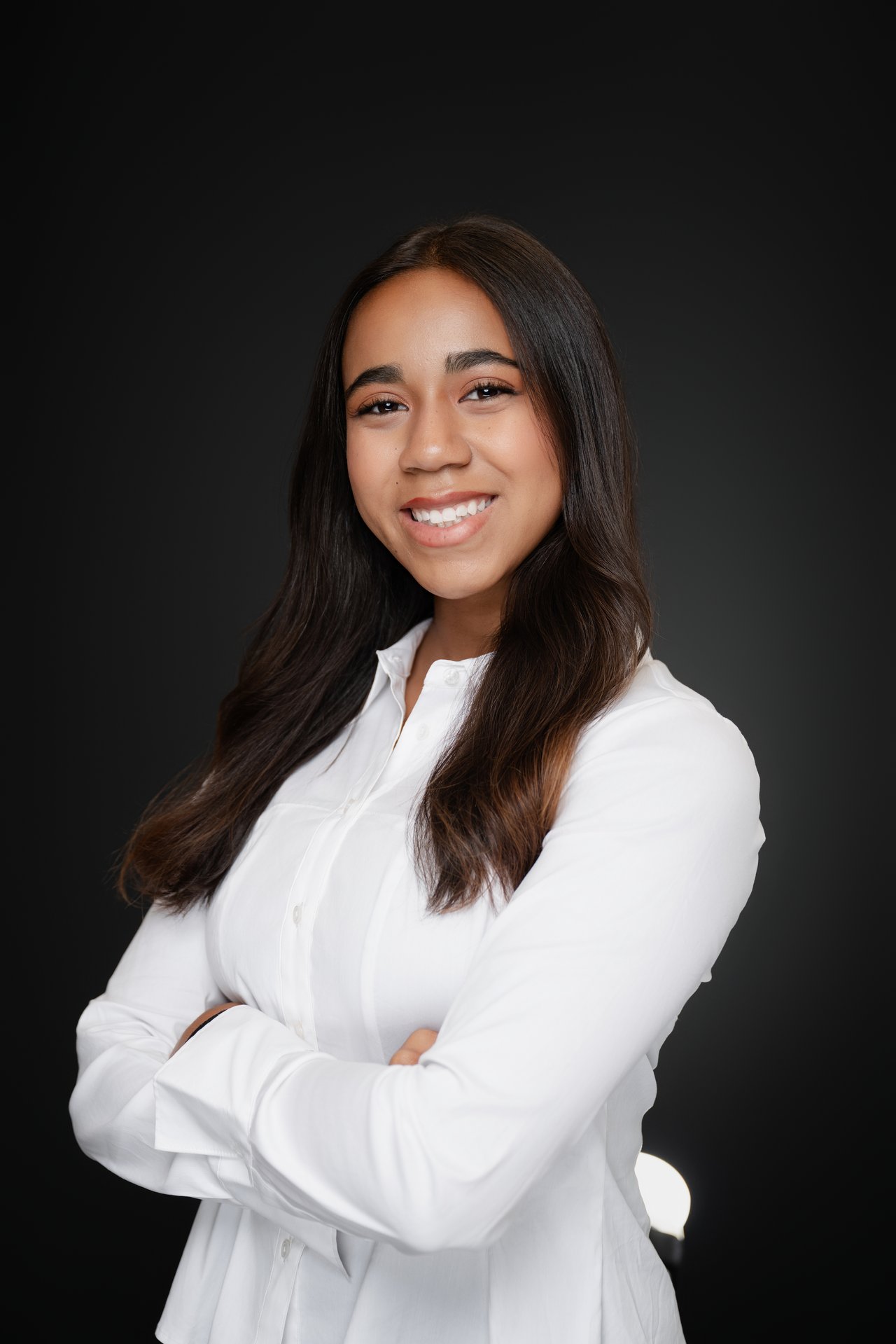 Viana Russell smiling with her arms crossed in a white blouse against a dark background.