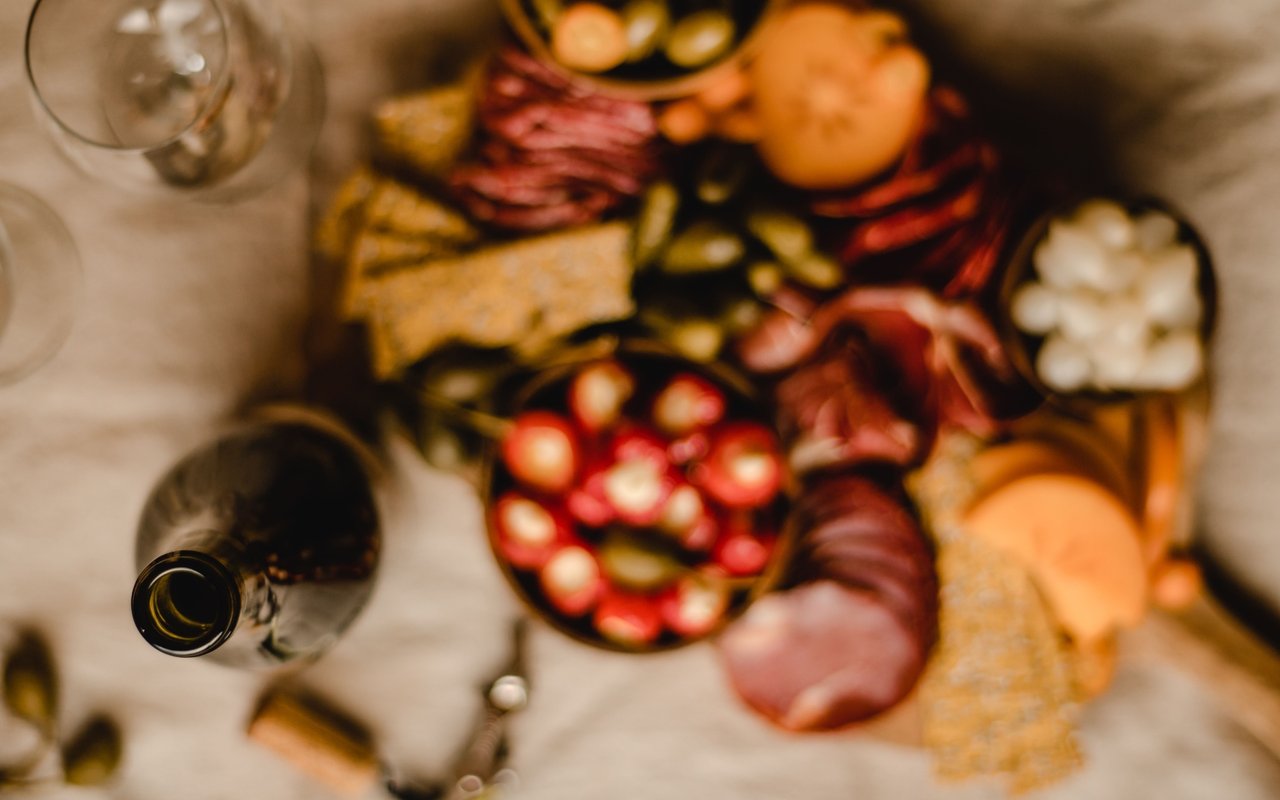 Charcuterie spread with cured meats, cheeses, crackers, fruit, and wine glasses.