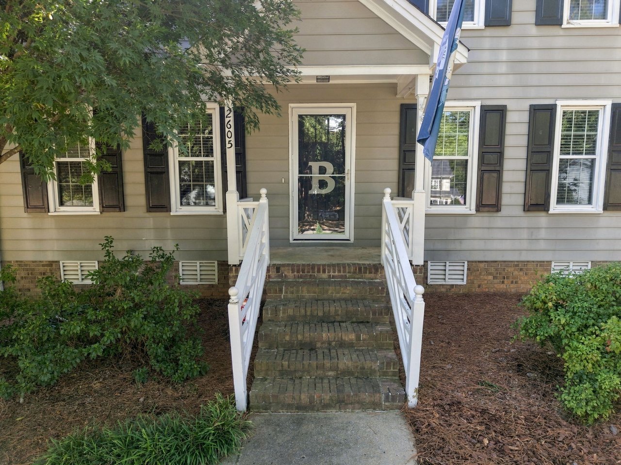 House entrance with brick steps, white railings, black shutters, and a blue flag.