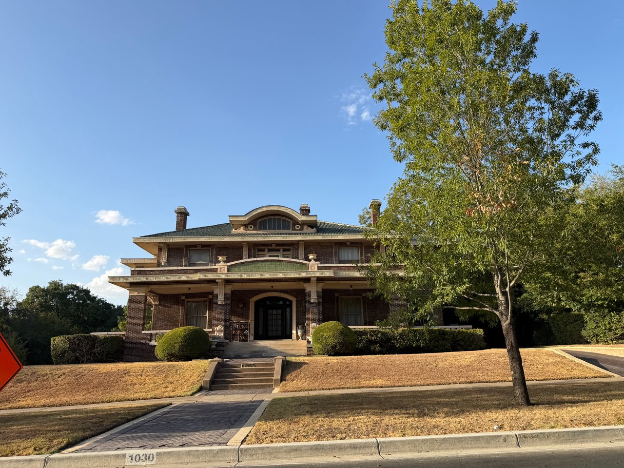 Historic two-story brick house with a broad porch, front steps, and a mature tree.
