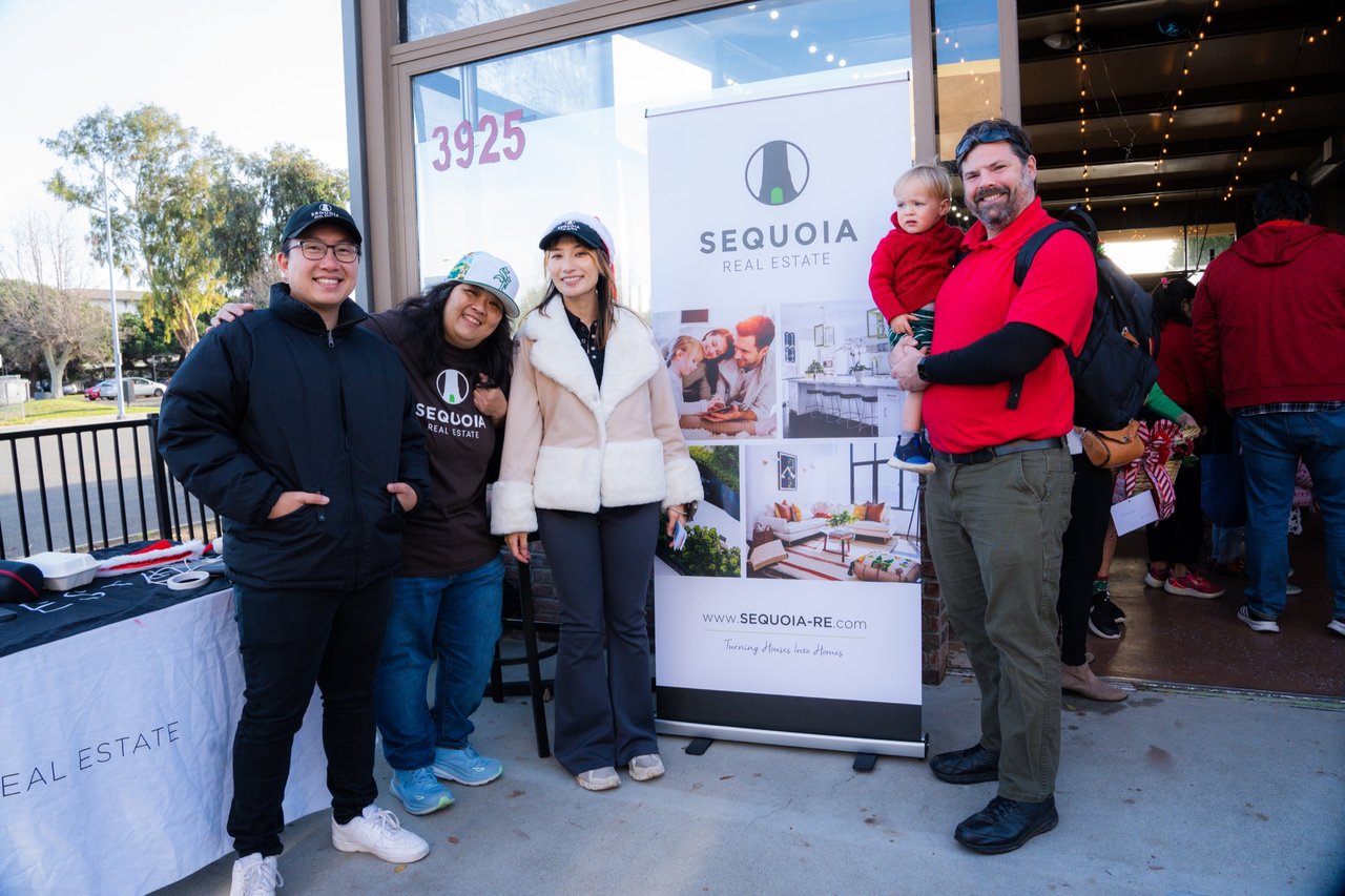 A group poses at a Sequoia Real Estate event; a man in red holds a baby beside the company banner.
