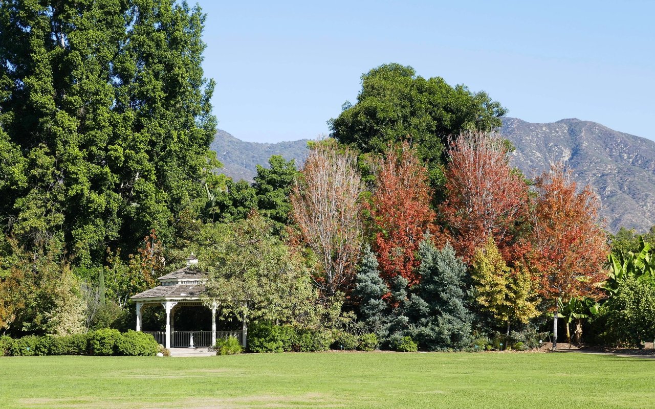 Park lawn and white gazebo framed by autumn trees, with mountains in the background.