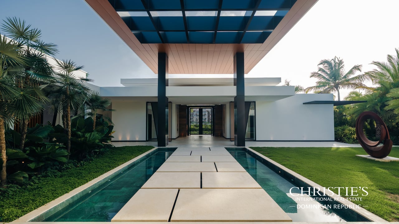 Modern villa entrance with a stone walkway over a reflecting pool and a timber-and-glass canopy.