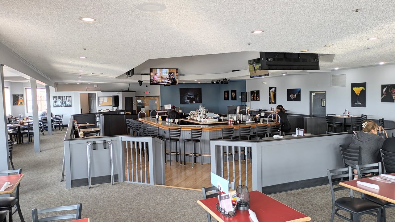 Restaurant interior with a curved bar, dining tables, and wall-mounted televisions.