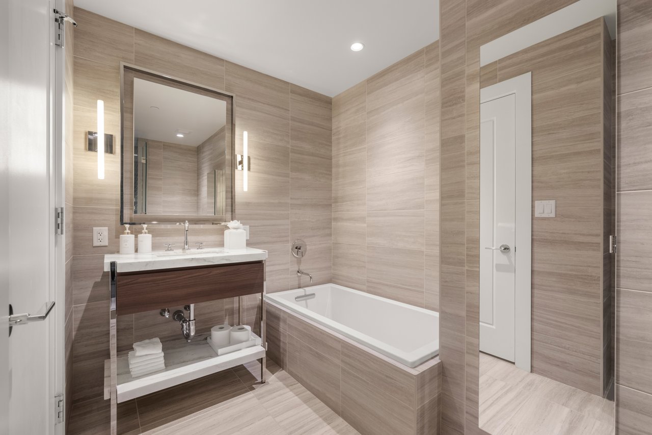 Modern tiled bathroom with a white bathtub and dark wood vanity beneath a large mirror.