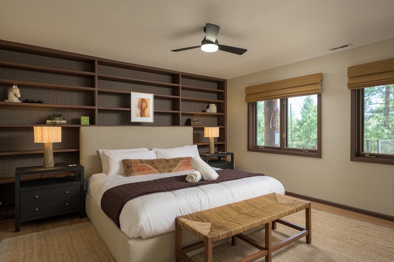Bedroom with a king-size bed, dark built-in shelving, and windows overlooking trees.