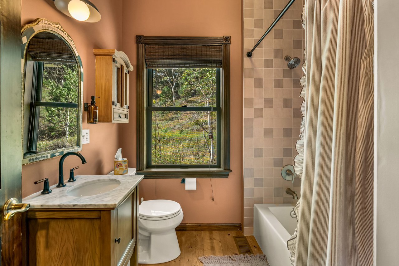 Bathroom with salmon-pink walls, a marble-topped wood vanity, and a window overlooking trees.