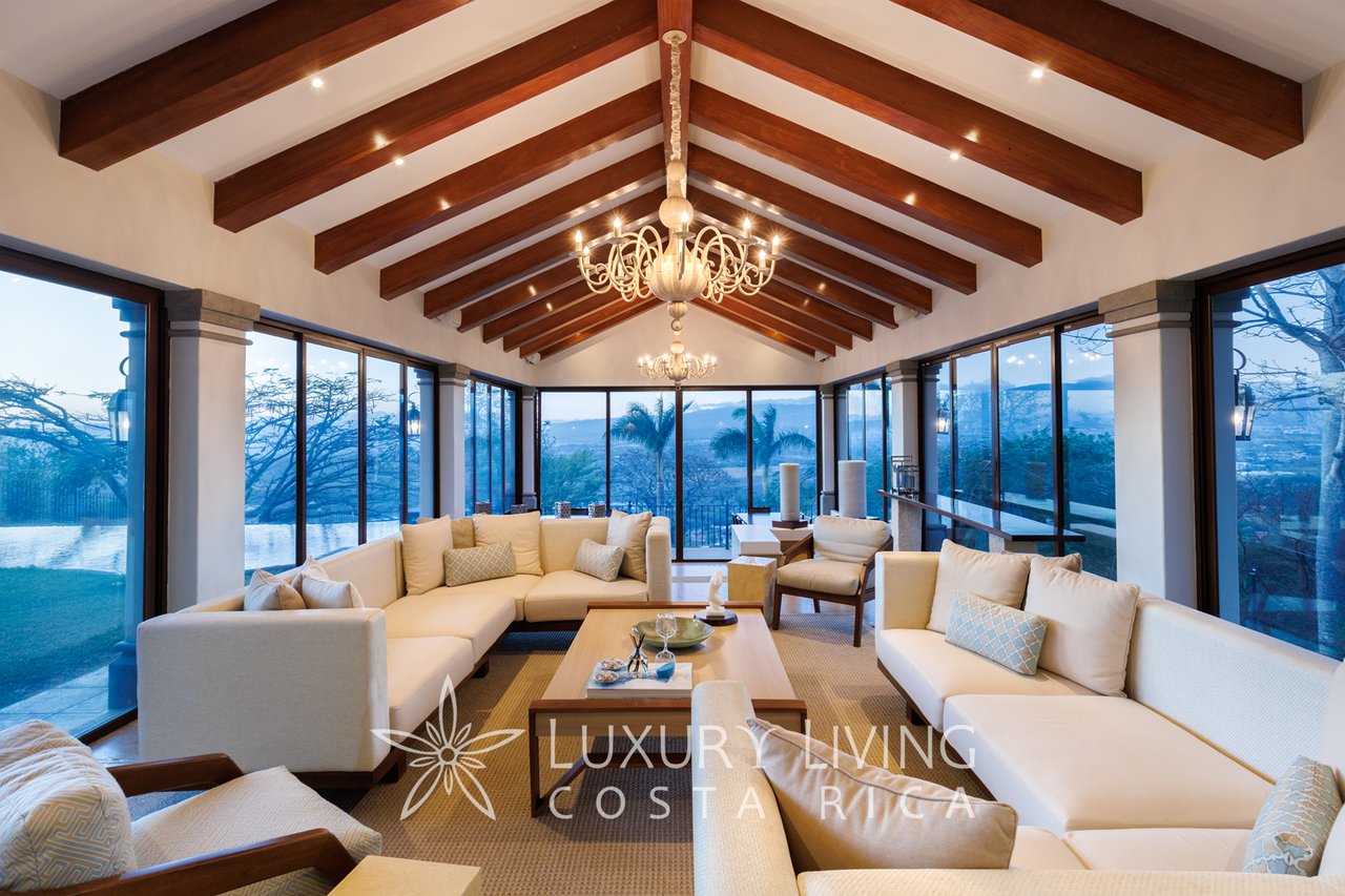 Living room with cream sectional sofas, exposed wooden ceiling beams, and floor-to-ceiling windows.