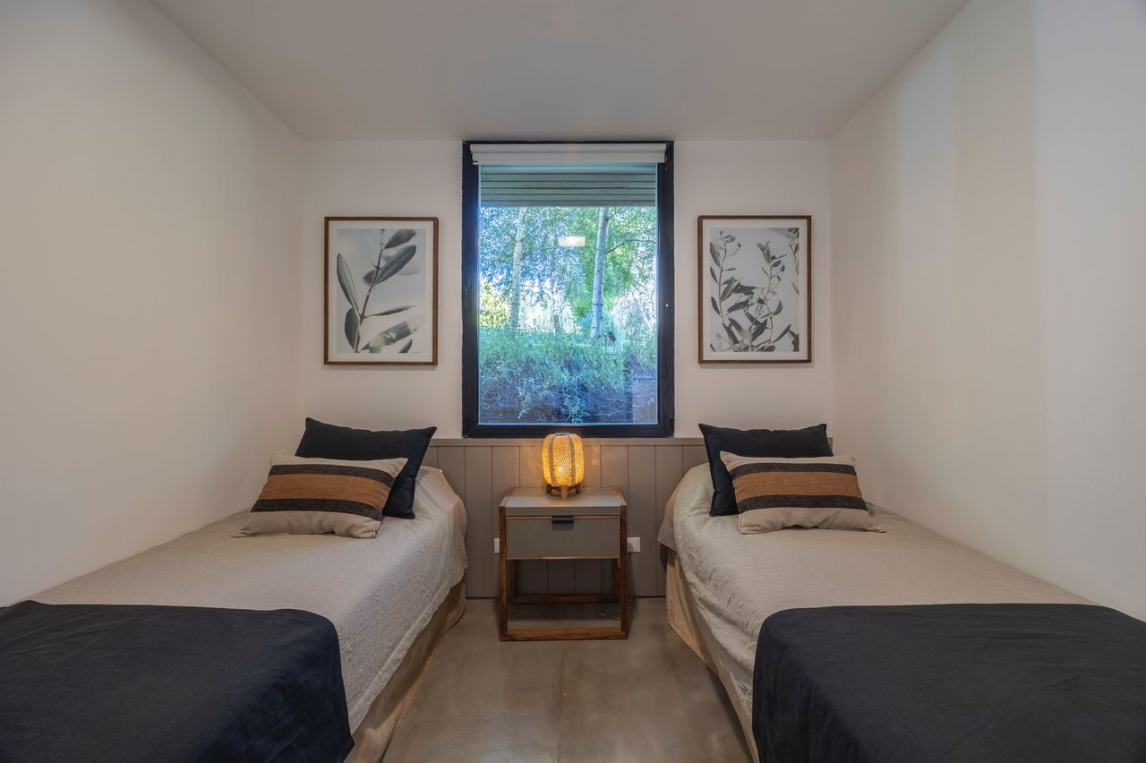 Twin bedroom with two single beds, botanical prints, and a window overlooking greenery.