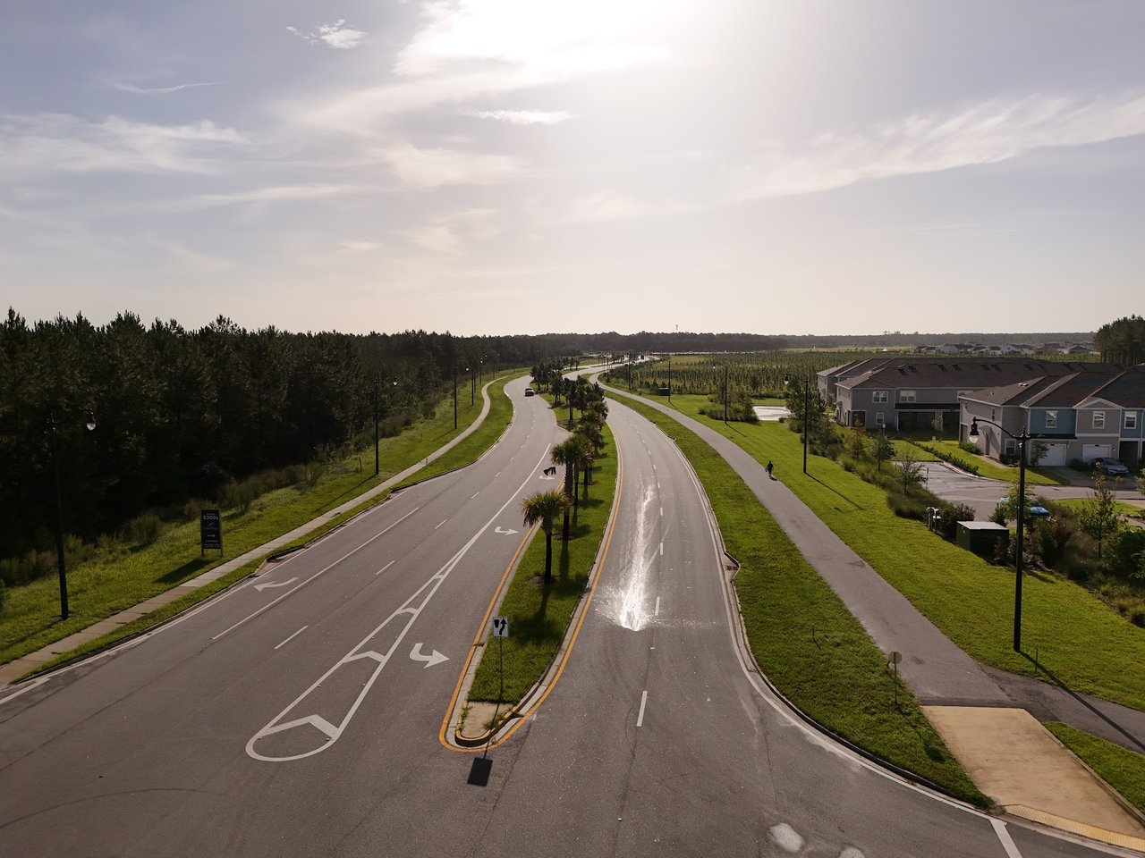Aerial view of a divided neighborhood road with landscaped medians, sidewalks, and homes.