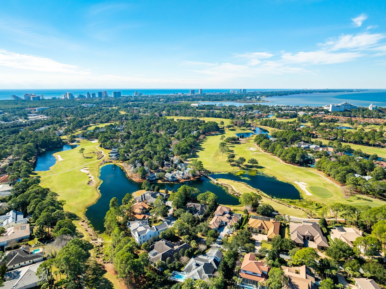 Aerial of Sandestin golf fairways wrapping blue lagoons and luxury pool homes with Choctawhatchee Bay beyond in Miramar Beach, Florida
