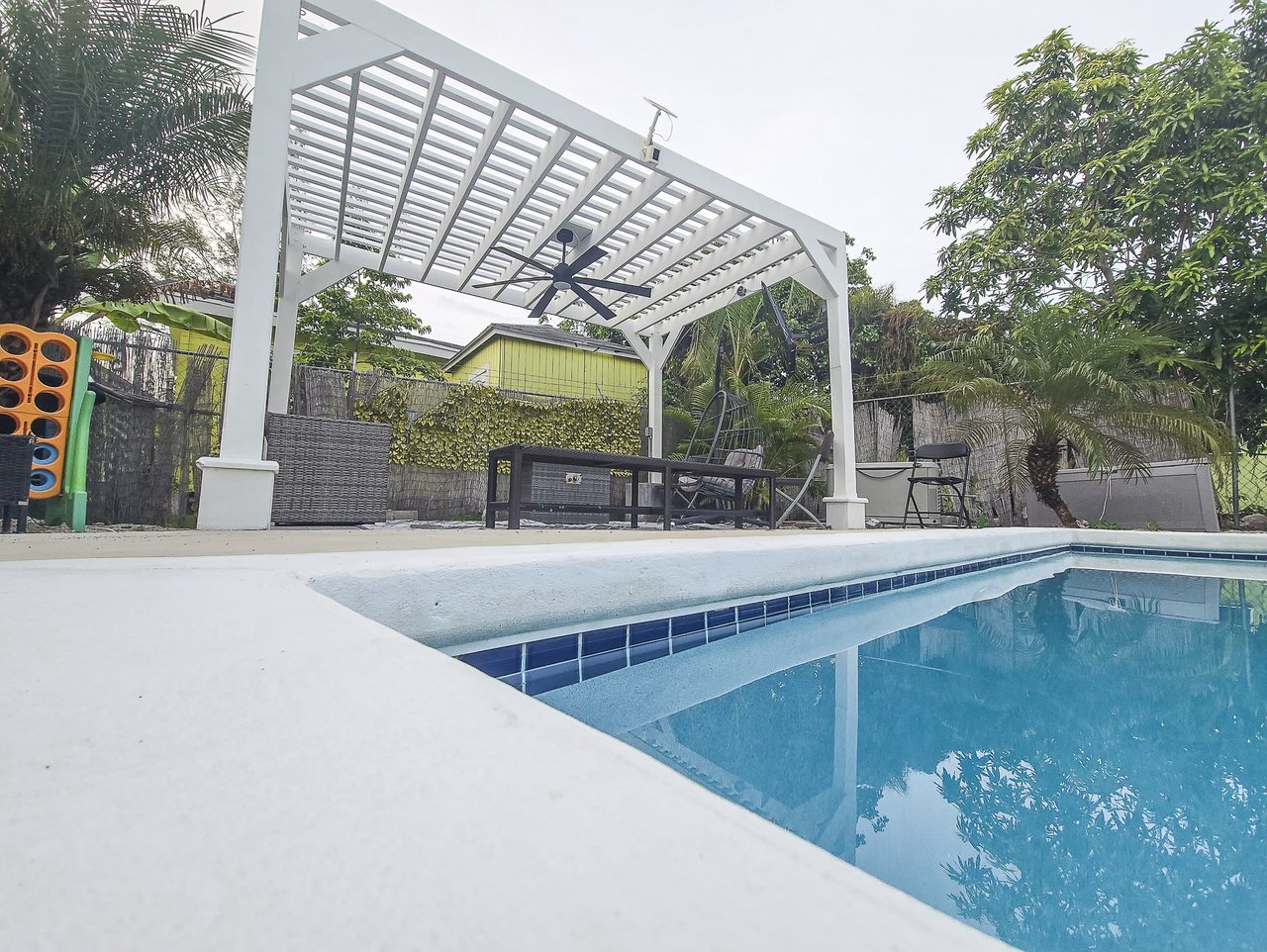 Swimming pool beside a white pergola-covered patio with outdoor seating.