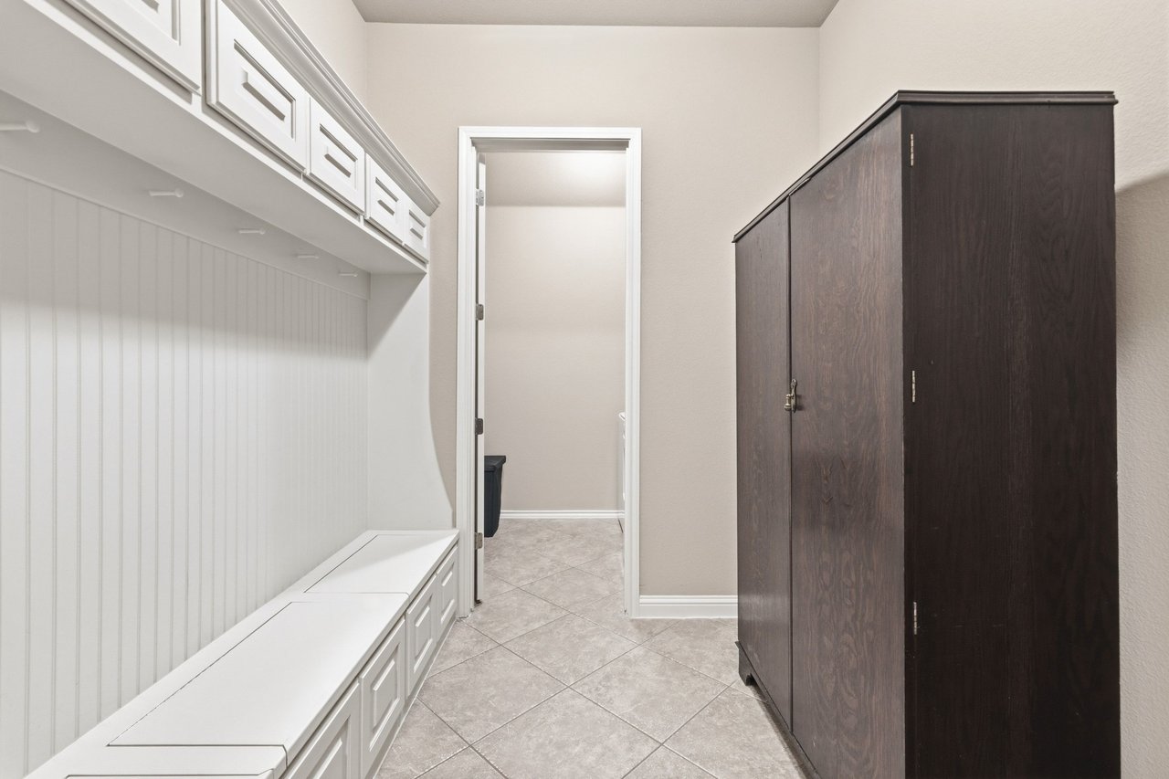 Mudroom with white built-in bench and cabinets, a tall dark wood cabinet, and tiled flooring.